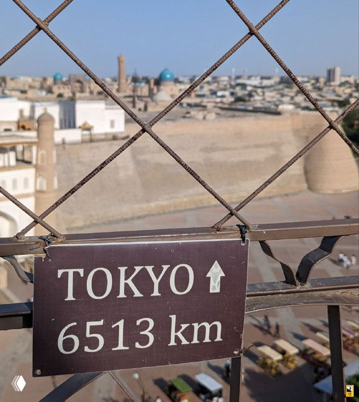 Знак TOKYO 6513 km на ограждении смотровой площадки Bukhara Tower: указатель направления и расстояния на фоне городской панорамы.
