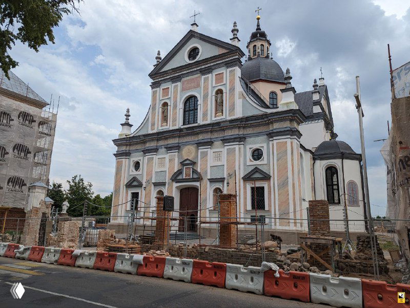 Фасад костела Божьего Тела в Несвиже во время реставрации: фронтон, апсида и элементы барочного декора на фоне облачного неба.