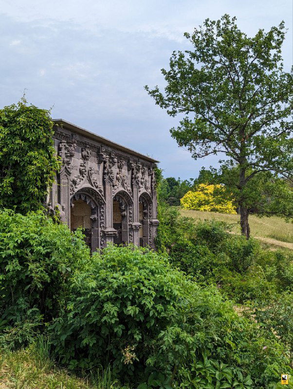 Декоративная каменная арка и заросли кустарника в ландшафте усадьбы Ореховно — деталь паркового декора на фоне деревьев.