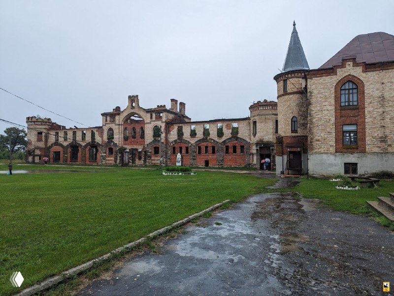 Вид на внутренний двор усадьбы Муромцево после дождя: ровный газон, дорожки и длинное кирпичное здание с башней и служебными пристройками.