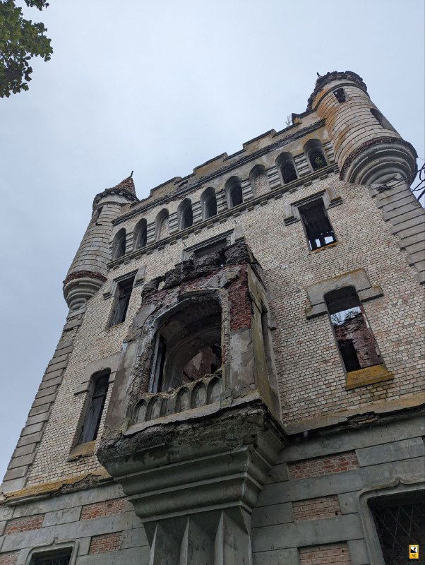 Высокая доминантная башня донжон и фасад усадебного дома «Замок мира», снятые снизу на фоне пасмурного неба, создают выразительную перспективу.