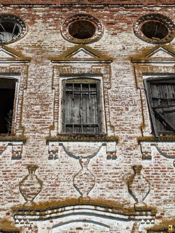 Фрагмент кирпичной стены церкви с оконными проёмами и декоративными узорами на фасаде; облупившаяся кладка и следы времени.