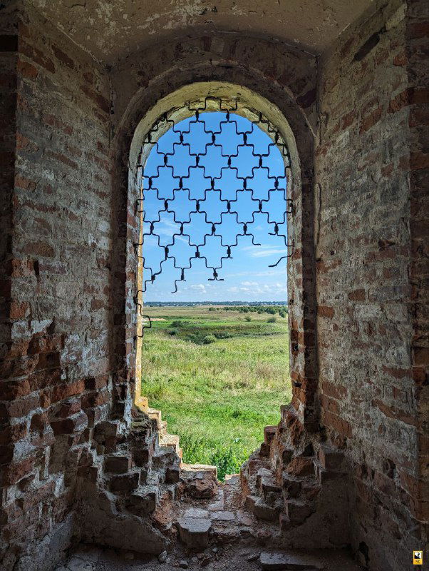 Окно с фигурной арочной решёткой в стене церкви, через которое открывается вид на суздальское ополье и дальние поля, рама без остекления.