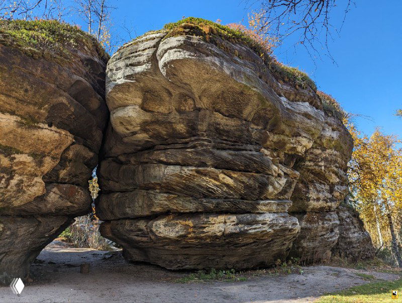 Крупный вид на слоистую скалу с округлыми выступами и небольшим пролётом между глыбами, осенние листья у основания и чистое небо.
