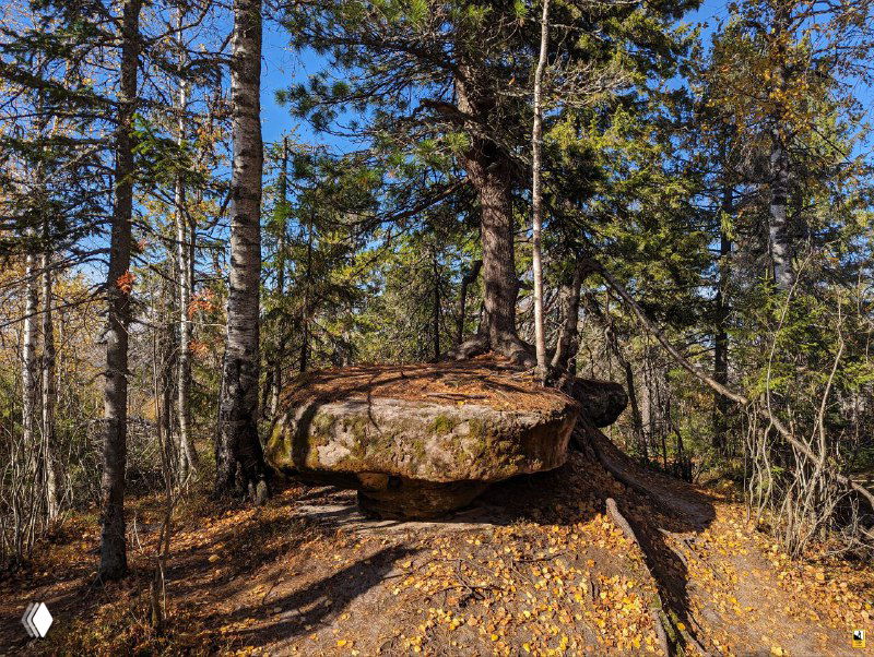 Низкая широкая плоская глыба словно стол, окружённая осенним лесом, травой и мягкой тенью на земле у подножия.