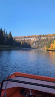 Вид с носа лодки по реке Усьва: плавный изгиб русла, спокойная поверхность воды и лесистые склоны в тёплых осенних оттенках за горизонтом.