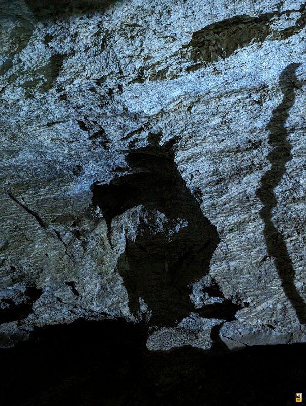 Силуэт на фоне подсвеченного свода пещеры; контраст тёмных углублений и белых известковых отложений подчёркивает масштаб подземной камеры в Кунгурской пещере.