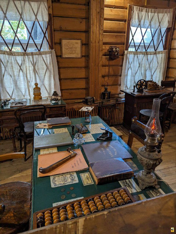 Музейный кабинет с письменным столом, абакусом, керосиновой лампой и документами, воссоздающий рабочее место учителя и административную обстановку того времени.