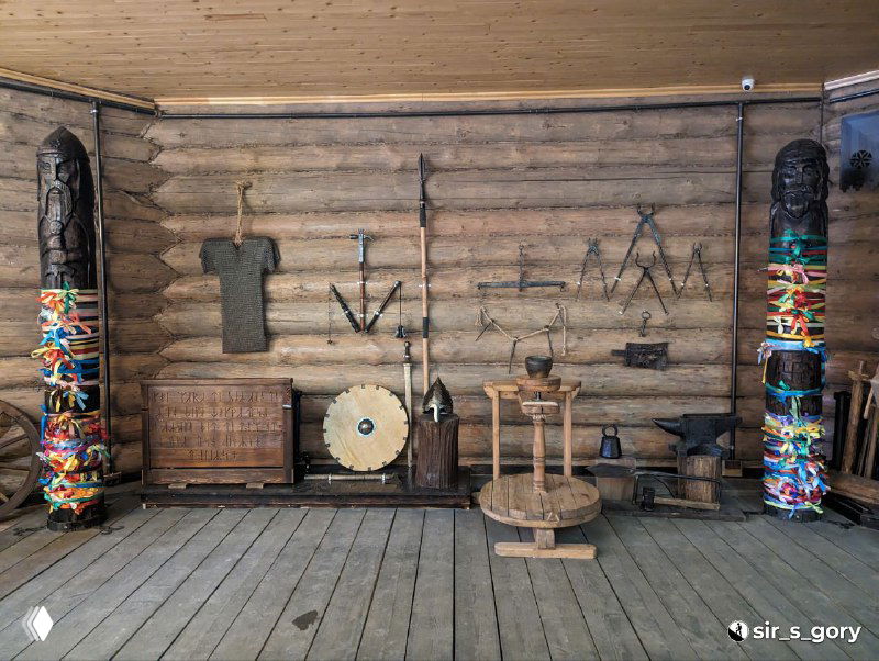 Интерьер терема: выставленные народные предметы — прялка, щит, инструменты и резные столбы как этнографическая экспозиция.