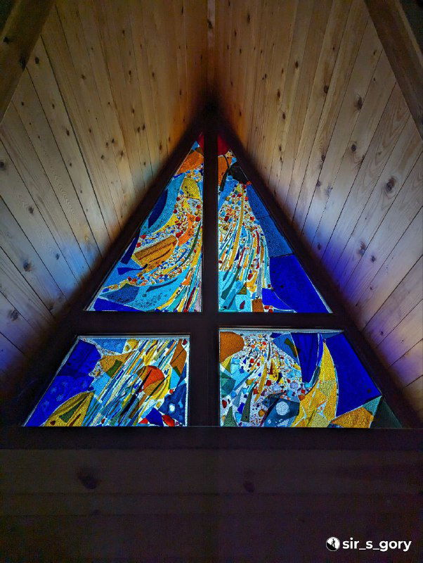 Треугольное витражное окно в верхнем ярусе терема: разноцветные стекла и декоративный орнамент, создающие мягкий внутренний свет.