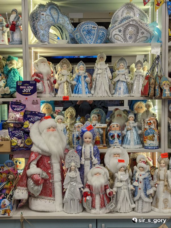 Витрина с коллекцией кукол и фигурок Снегурочки и Деда Мороза в сувенирном магазине — множество ручных изделий и фабричных сувениров.