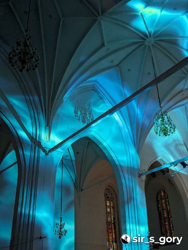 Часть потолка и арок собора, залитые голубыми и бирюзовыми прожекторами, подчёркивающими готическую архитектуру во время музыкального номера.