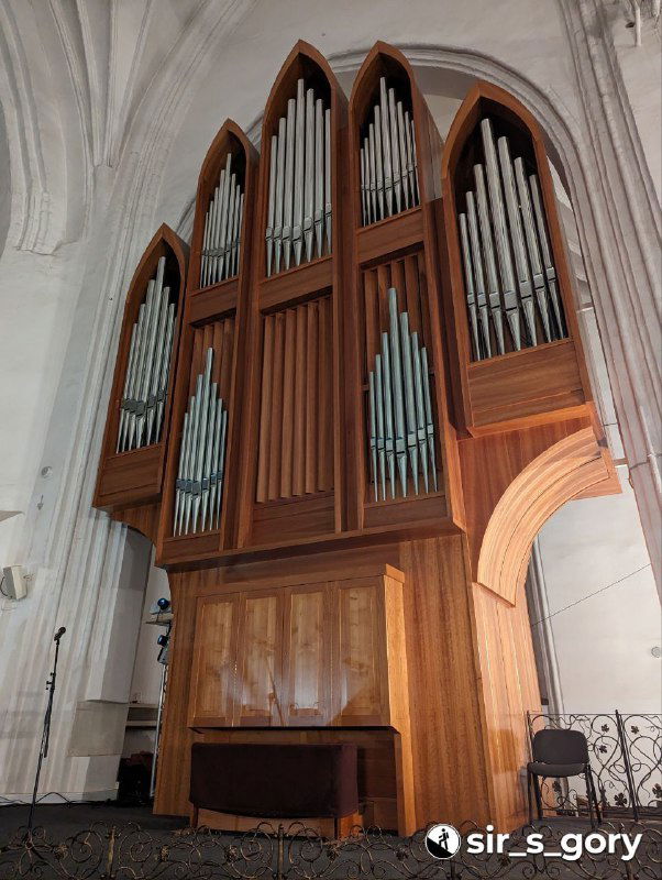 Деревянные трубы органа крупным планом: часть корпуса инструмента с деревянной отделкой и вертикальными металлическими трубами на фоне стены.