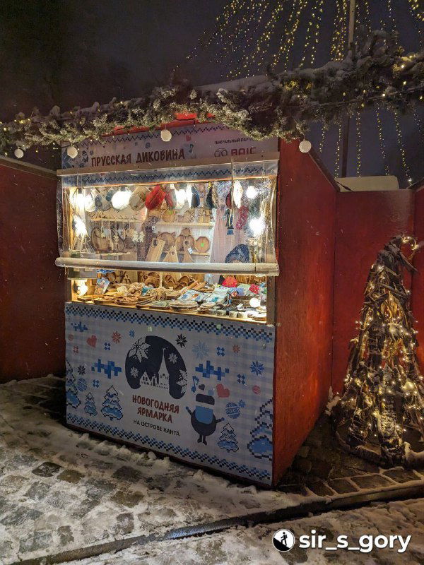 Небольшая торговая лавка с снежным фонарём и ассортиментом уличной еды и угощений; огни и декоративные элементы создают праздничное настроение.