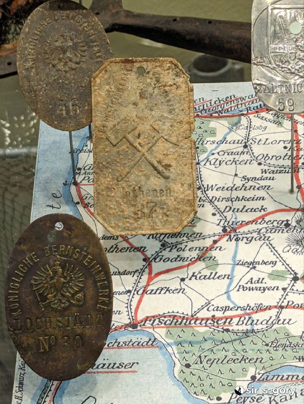 Исторические медальоны и жетоны на фоне старой карты региона — сопутствующие музейные предметы, связанные с историей края.