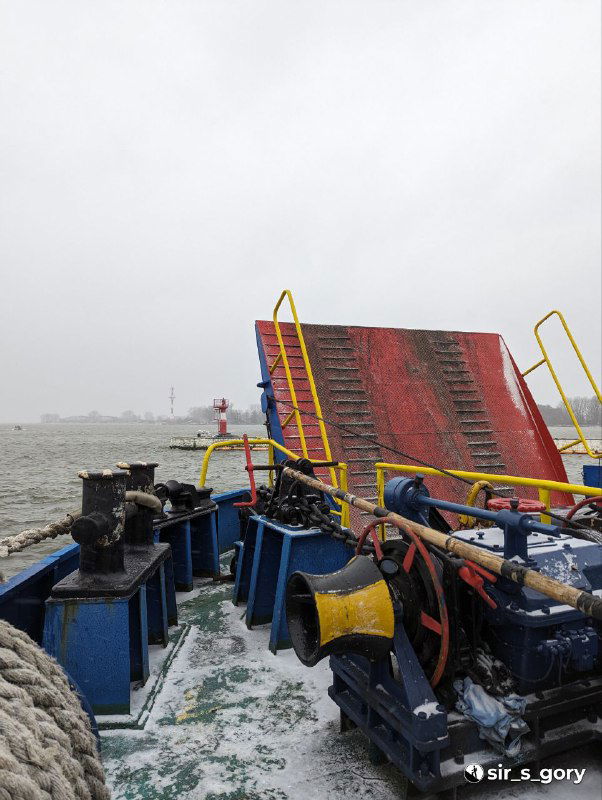 Палуба парома со скользким покрытием и забором пандуса: вид на шлюпку и серое Балтийское море в снежную погоду