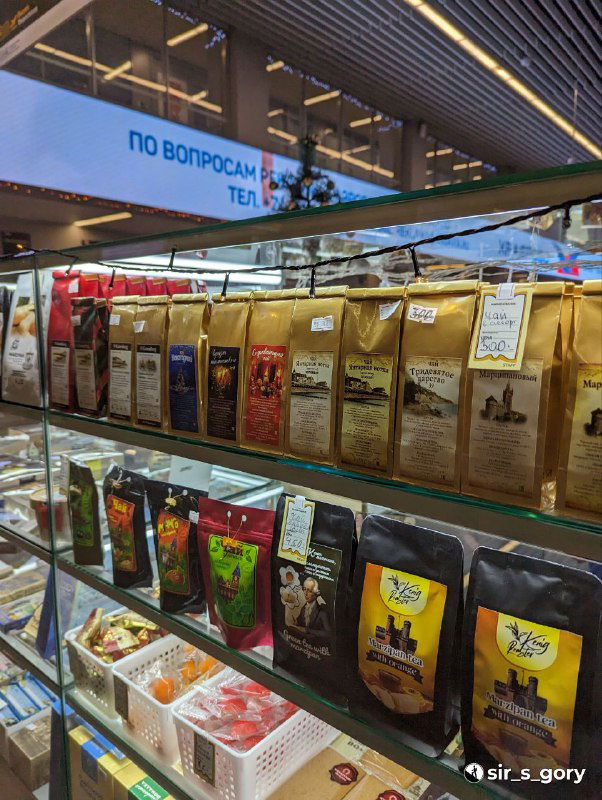 Полки в магазине с разными упаковками сувениров и продуктовых подарков: кофе, специи и сладости в пакетах — вид в торговом отделе сувениров.