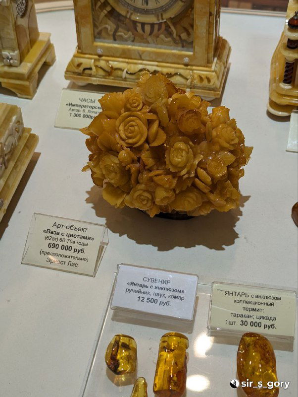 Витрина с изделиями из янтаря: сувениры, статуэтки и ценники, крупный кусок янтаря и ценовые бирки — музейно-магазинный экспонат.