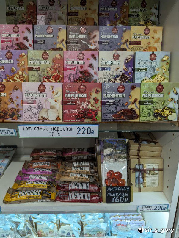 Ряды коробок и упаковок с маркированными названиями сладостей и сувениров: витрина с ассортиментом на прилавке магазина городского центра.