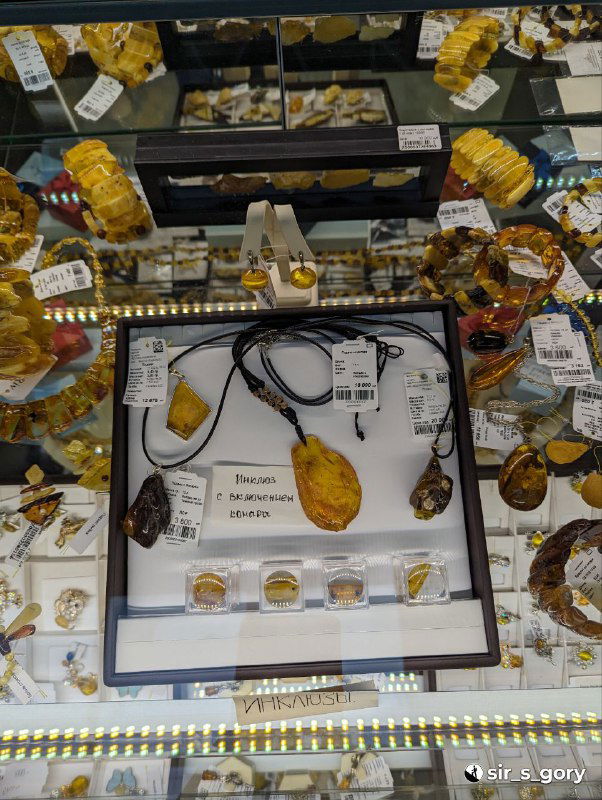 Показаны подвески и украшения с янтарными вставками на чёрном фоне витрины, комплект украшений для продажи в ювелирном отделе сувенирного магазина.