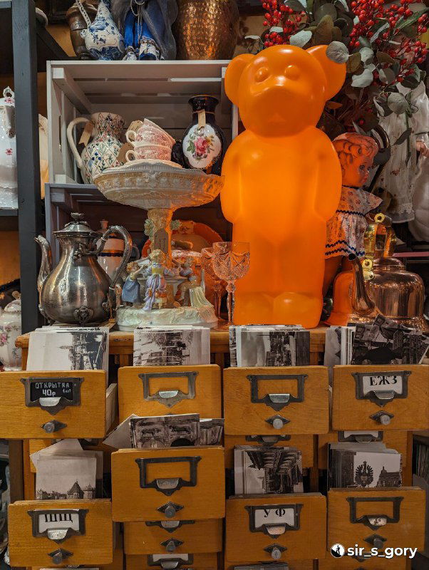 Оригинальная витрина с ярко-оранжевой фигурой в виде медведя и другими сувенирами: декоративная композиция в магазине подарков.