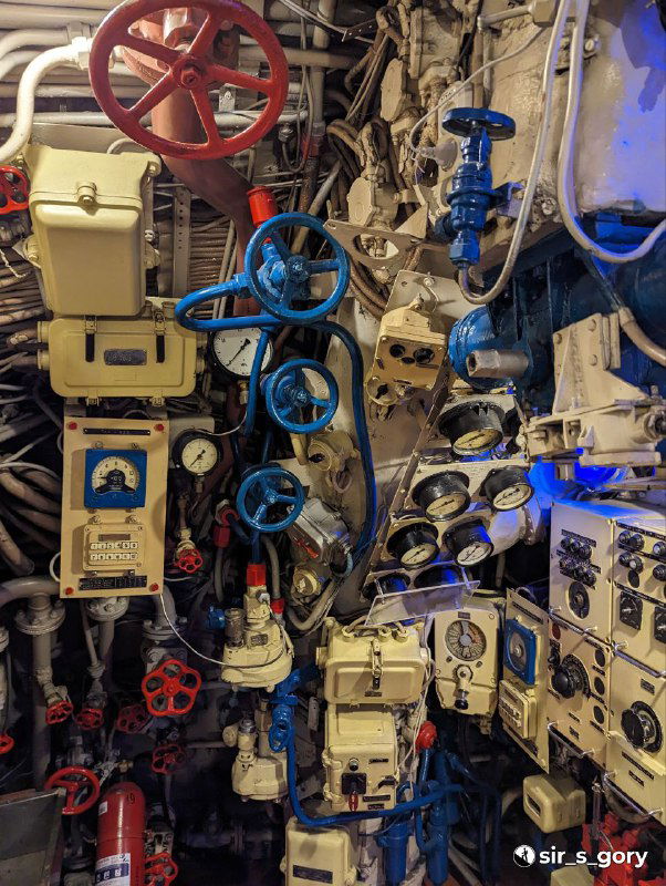 Скопление вентилей, рукояток и приборных панелей в одном из отсеков подводной лодки — демонстрация плотной механической компоновки и систем управления.