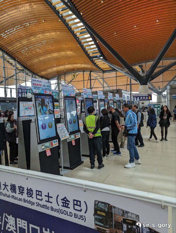 Внутреннее пространство терминала паромов или автобусов с деревянным потолком: люди у информационных киосков и указатели направления движения пассажиров.