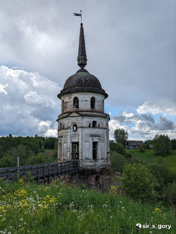 Колокольня или шатровая башня на холме у реки, полуразрушенная, со старой деревянной лестницей и зарослями вокруг — вид типичной тотемской архитектуры.