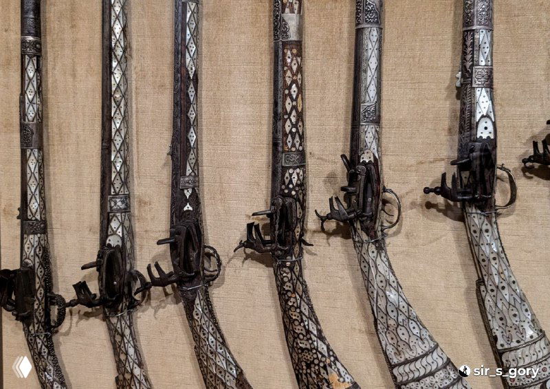 Ряд старинных ружей и мушкетов с инкрустацией и богато украшенными прикладами, выставленных на стене Морского музея в Которе.