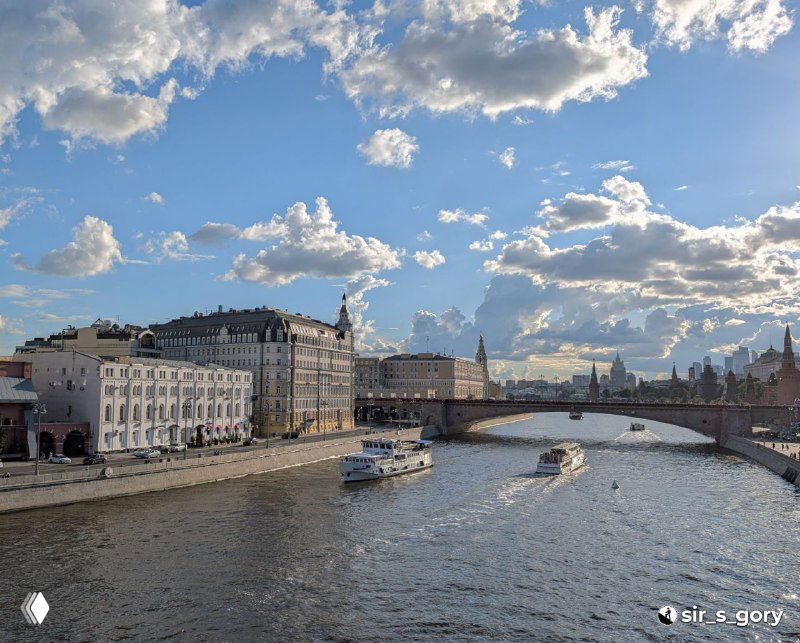 Вид на Москву‑реку и набережную рядом с Зарядьем: прогулочные катера, река, городская архитектура и широкое небо с живой облачностью
