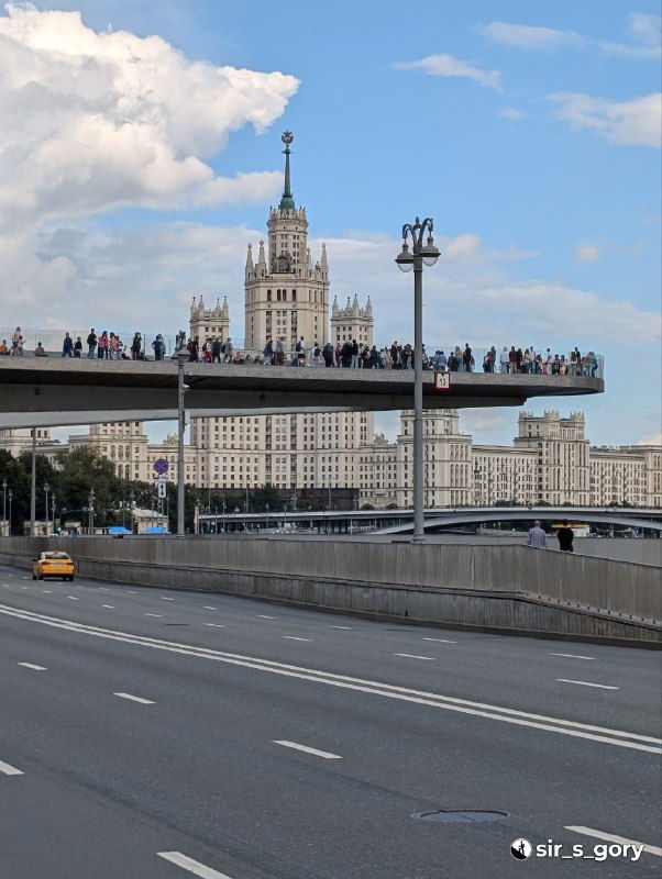 Парящий мост в Зарядье с множеством людей на смотровой площадке и высотным зданием на заднем плане — зрелищный городской пейзаж