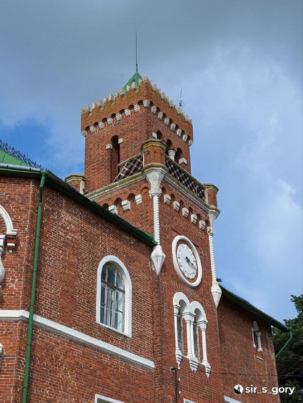 Высокая квадратная башня с часами на фасаде и небольшими арочными окнами; заметны следы времени и реставрационные участки кирпичной кладки.