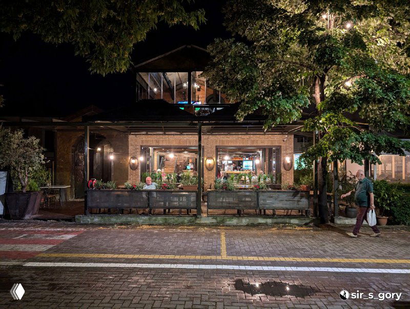 Ночная фотография фасада ресторана у набережной в Поградеце: подсветка веранды, деревья, тротуар и спокойная атмосфера вечера на озере.