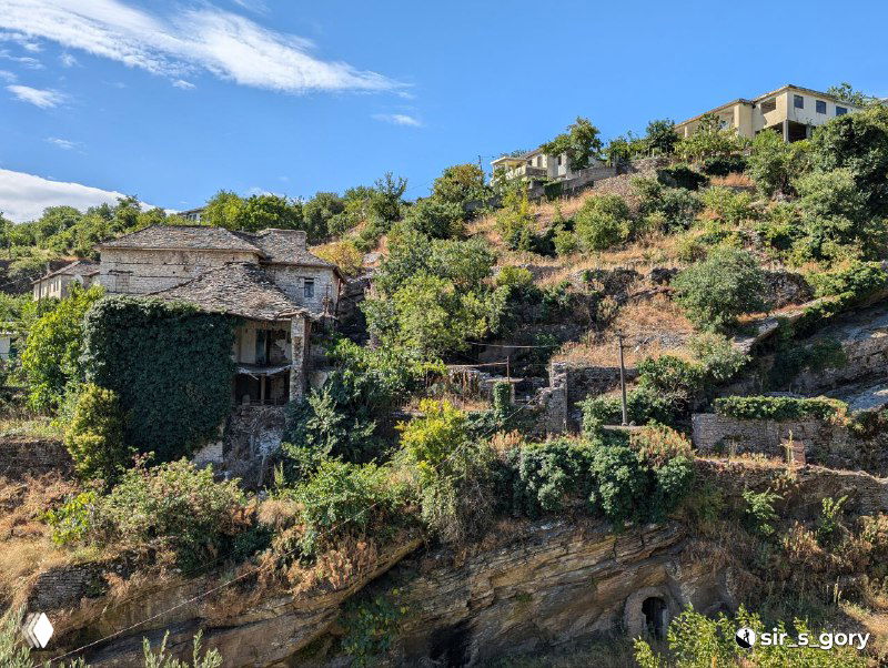 Террасированные холмы и заброшенные дома в окрестностях Гирокастры, заросшие растительностью каменные участки и остатки старых построек.