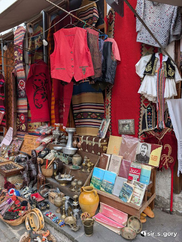 Прилавок с национальной одеждой красно‑чёрной гаммы, коврами, мелкими сувенирами и турецкой посудой, крупный план рыночной витрины.