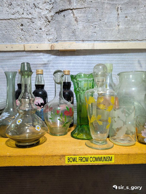 Полка с винтажными стеклянными вазами и графинами в этнографическом музее, одна полка подписана «BOWL FROM COMMUNISM», коллекция бытовых предметов.