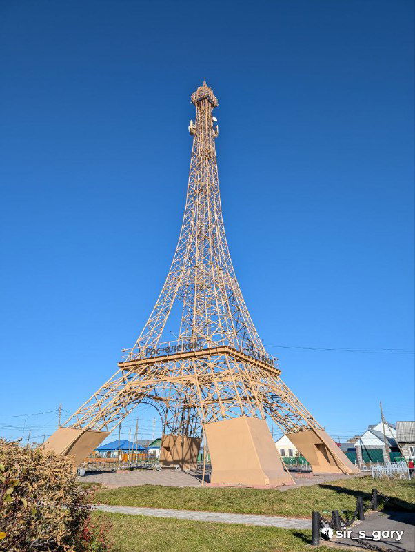 Фрагмент металлической конструкции, имитирующей Эйфелеву башню, поднятой в селе Париж — вид на декоративную башню и небо над деревней.