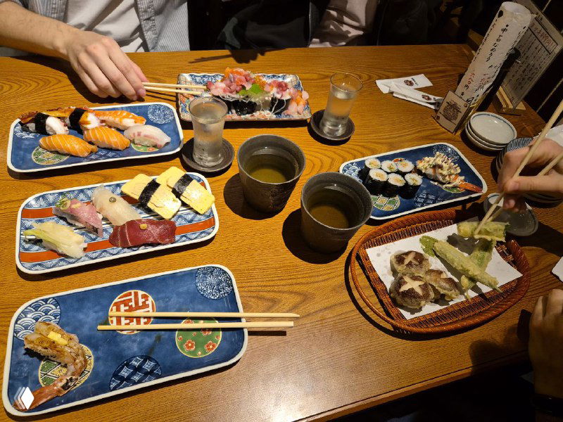 Стол с несколькими тарелками суши, роллами и напитками в традиционном японском ресторане — кадр, показывающий локальную кухню и атмосферу ужина.