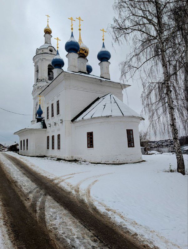 Варваринская церковь зимой: белые стены и синие купола, дорожка и берёзы в снегу на фоне реки у Музея пейзажа.