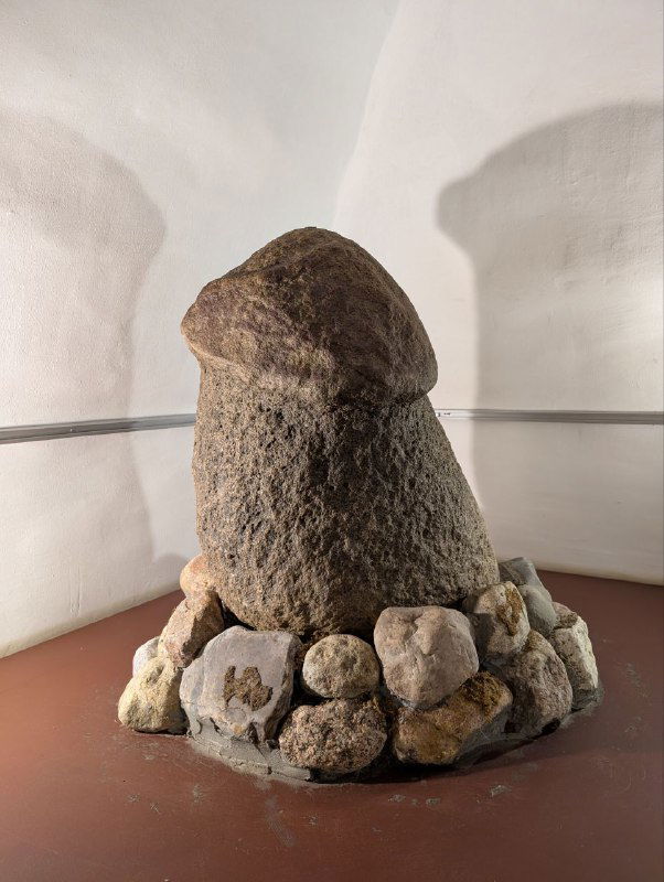 Экспонат музея «Древний Плёс и Ивановская земля» — каменный артефакт фаллической формы, выставлен в стеклянной витрине с подпором из гальки.