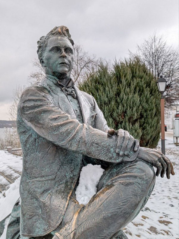 Памятник Исааку Левитану на фоне набережной и хвойных кустов, скульптура художника в зимнем парке Плёса у Волги.