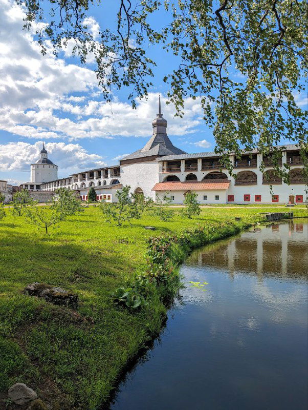 Белокаменный монастырь у зеркального пруда в тёплое время года; отражение строений в воде, зелёные насаждения и спокойный культурный пейзаж, снимок из серии.