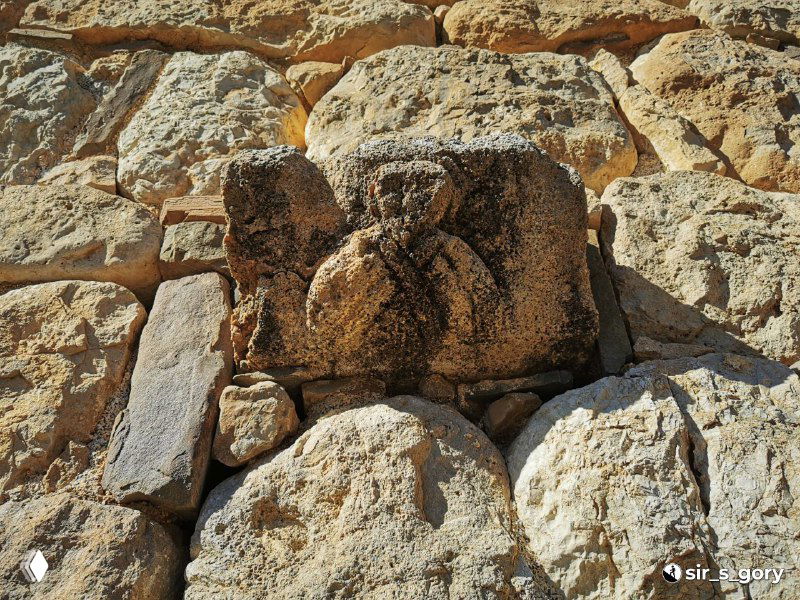 Фрагмент каменной кладки с резным камнем-орнаментом у основания стены Тхаба-Ерды; видны следы обработки и погодного износа.