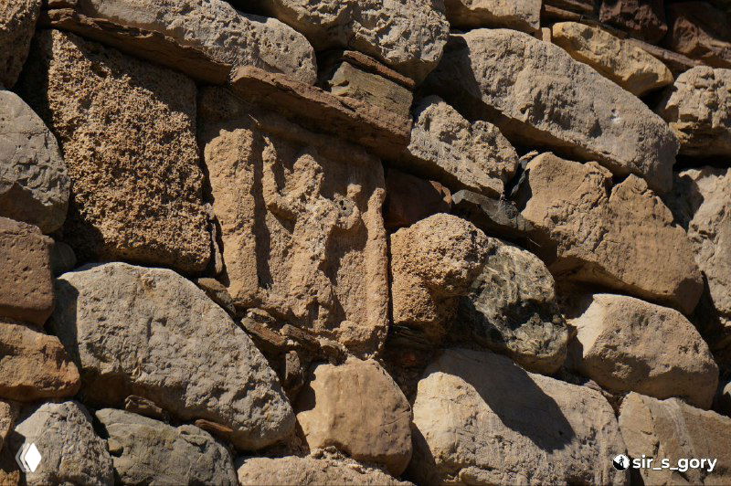 Деталь каменной кладки с мелкими рельефными элементами и рядом лежащими обломками; текстура камня хорошо читается на снимке.