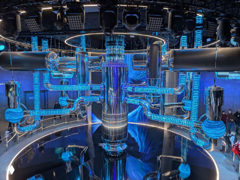 Центральный интерактивный модуль с подсветкой и трубопроводами в виде реактороподобной инсталляции, видна обзорная галерея и ограждения.