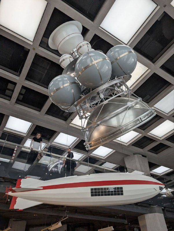 Макет корабля или подводного аппарата под потолком выставочного зала, шарообразные модули и крупный плавающий макет в масштабе экспозиции.