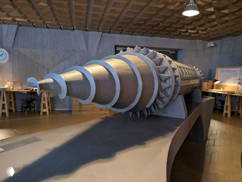 Гигантская модель технической установки на полу музея — цилиндрическая конструкция с видимыми спиралевидными элементами и крупномасштабным исполнением.