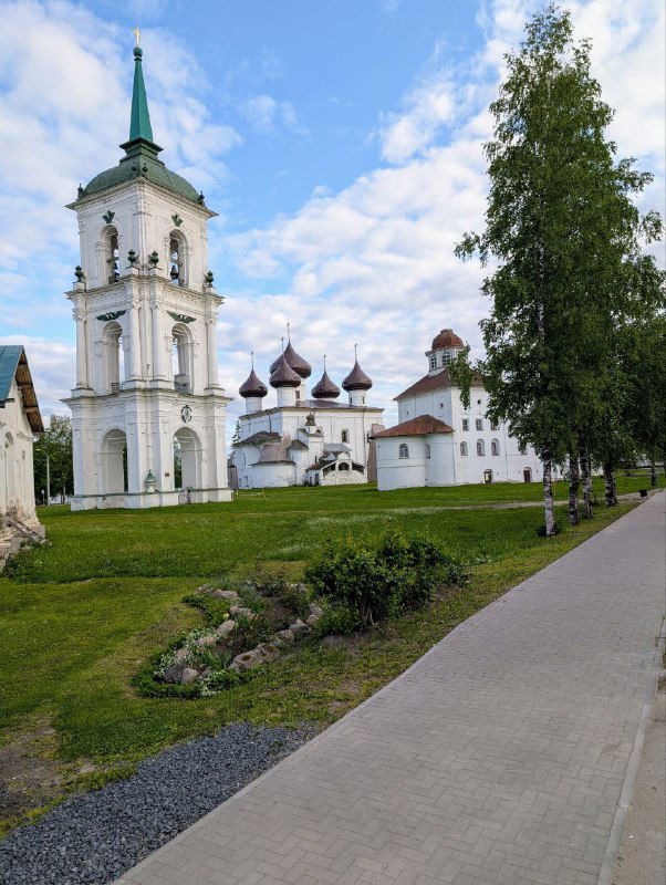 Панорамный вид на Соборную площадь и колокольню Каргополя вдоль тротуара, где соседствуют каменные и деревянные постройки в летнем свете.