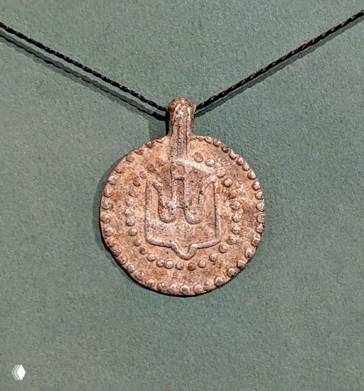 Медальон-подвеска XI века в музейной витрине: металлический амулет с орнаментом, обнаруженный при археологических раскопках в округе.
