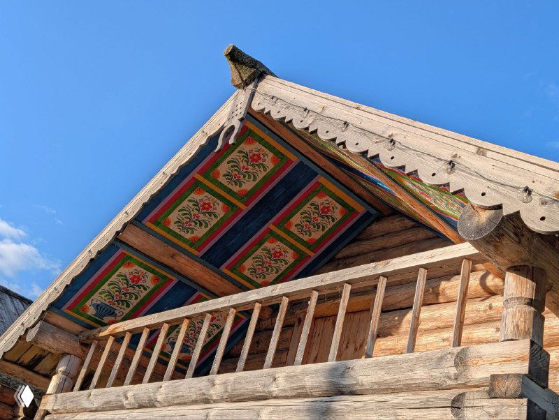 Ярко раскрашенный фронтон с балконом: насыщенные цвета, резные элементы и традиционный северный орнамент на фоне чистого неба